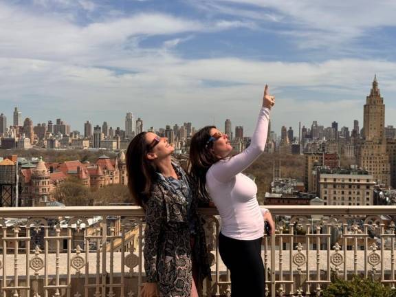 One woman points to the sky shortly after 2 p.m. as the moon slowly starts to block out the sun enroute to an eclipse of about 90 percent of the sun. They were on a rooftop party at a penthouse listed for sale for Photo: Heather Stein