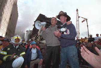 Standing on top of a crumpled fire truck with retired New York City firefighter Bob Beckwith, President George W. Bush rallies firefighters and rescue workers Friday, Sept. 14, 2001, during an impromptu speech at the site of the collapsed World Trade Center towers.