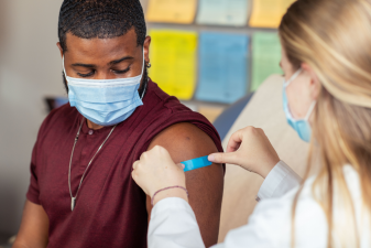A healthcare provider places a bandage over a patient’s flu vaccine injection site.