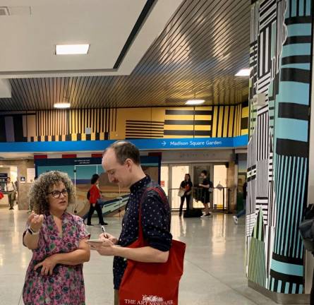 Artist Shoshanna Weinberger explains her Art at Amtrak work “Traveling Along Horizons” to a journalist at the press showing. Over Weinberger’s shoulder are colors reflecting a bright day; to her left, columnar art noting silently how women are holding up civilization. The bars and stripes behind her represent social divisions. Photo: Ralph Spielman