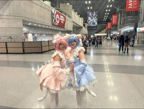 Two cosplayers dressed as the twin maids Ram and Rem from “Re:Zero” stand arm-in-arm in frilly pink and blue outfits at Anime NYC at the Javits Convention Center.