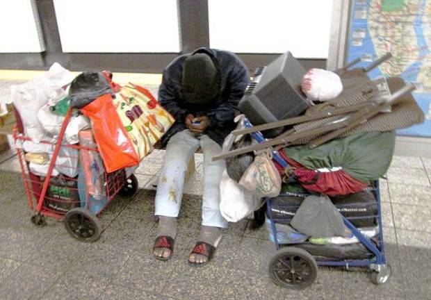 <b>Homeless person hunched over a cellphone with belongings in two shopping carts on a platform along the A line</b>. Photo: Wikimedia Commons