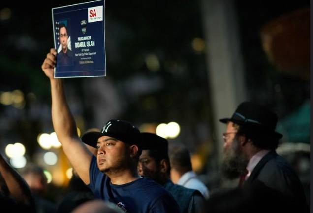 A mourner at the prayer vigil in Bryant Park on July 29 holds aloft a photo of Didarul Islam, the NYPD officer who was working as a security guard when he became victim No. 1 of crazed gunman Shane Tamura.