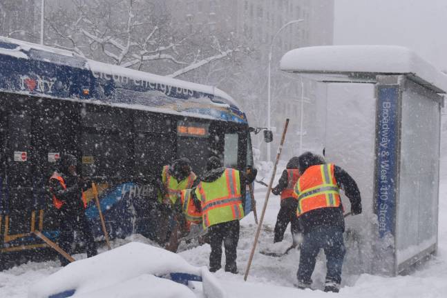 Workers clear snow trying to get a stuck bus moving again.