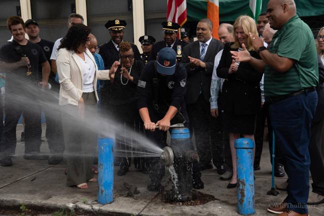 Multiple community leaders, including NYPD Commissioner Tisch, step back and applaud as the fire hydrant opens.