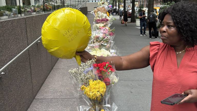 Woman holds a yellow balloon with a handwritten note, “LOVE ONE ANOTHER,” on July 31 on the growing makeshift memorial outside 345 Park Ave., where a gunman killed four innocent people and then took his own life on July 28.